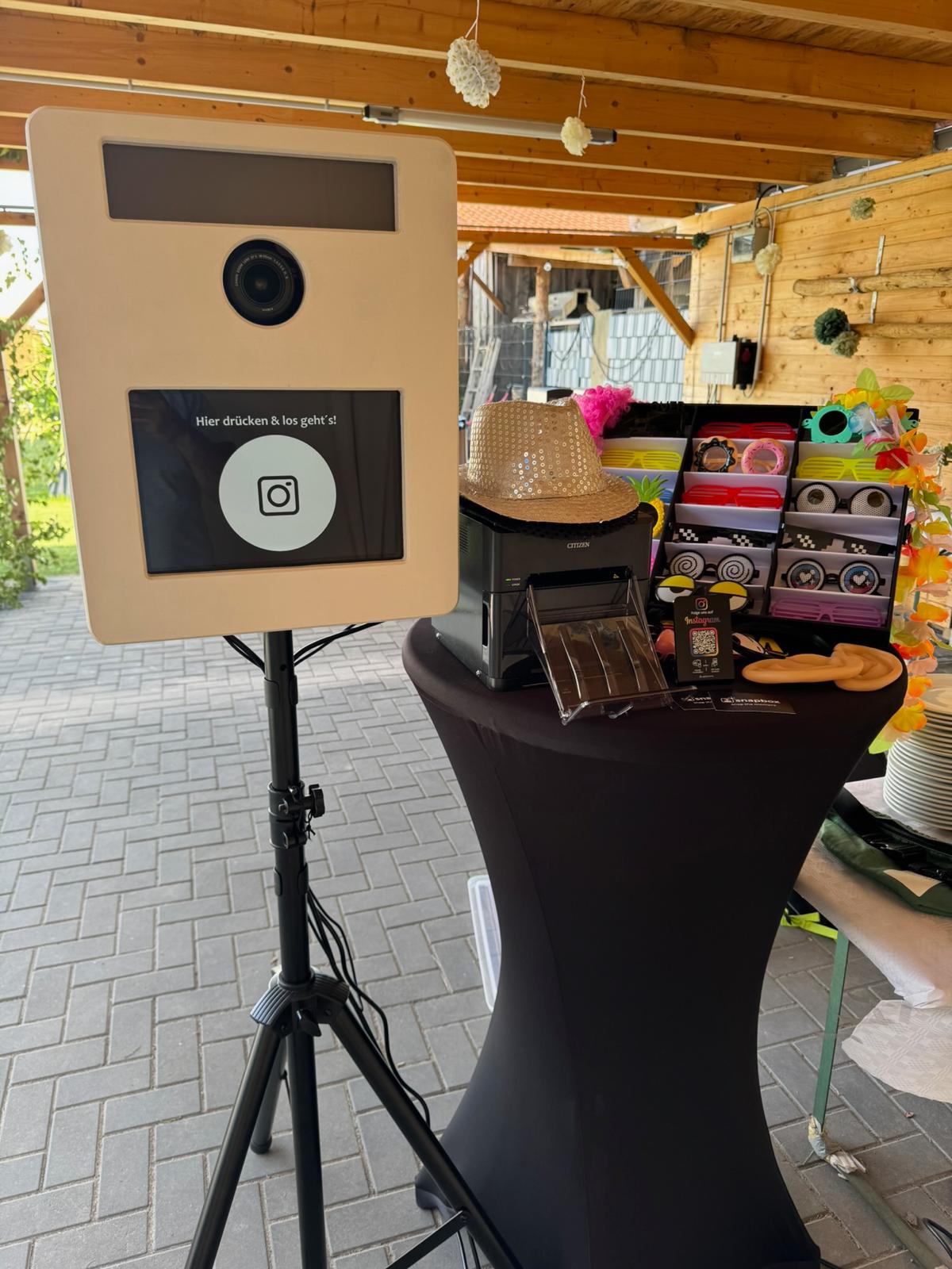Weiße GrinseLinse Fotobox mit Sofortdrucker und Accessoires auf einer Gartenfeier